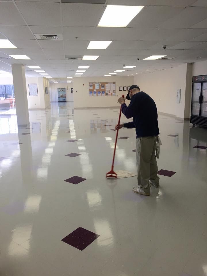 Person mopping a large, shiny floor with maroon diamond inlays in a building with fluorescent lights.