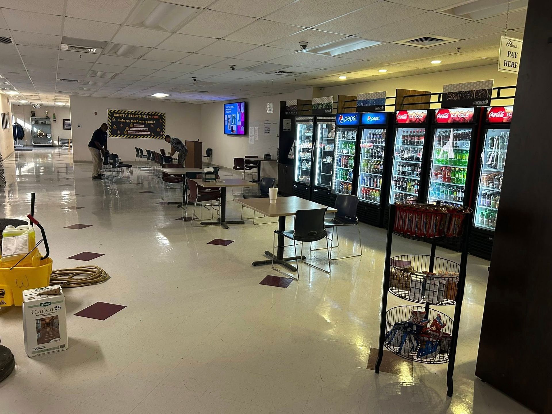 Interior of a hallway with vending machines, tables, a person cleaning, and a mop bucket.