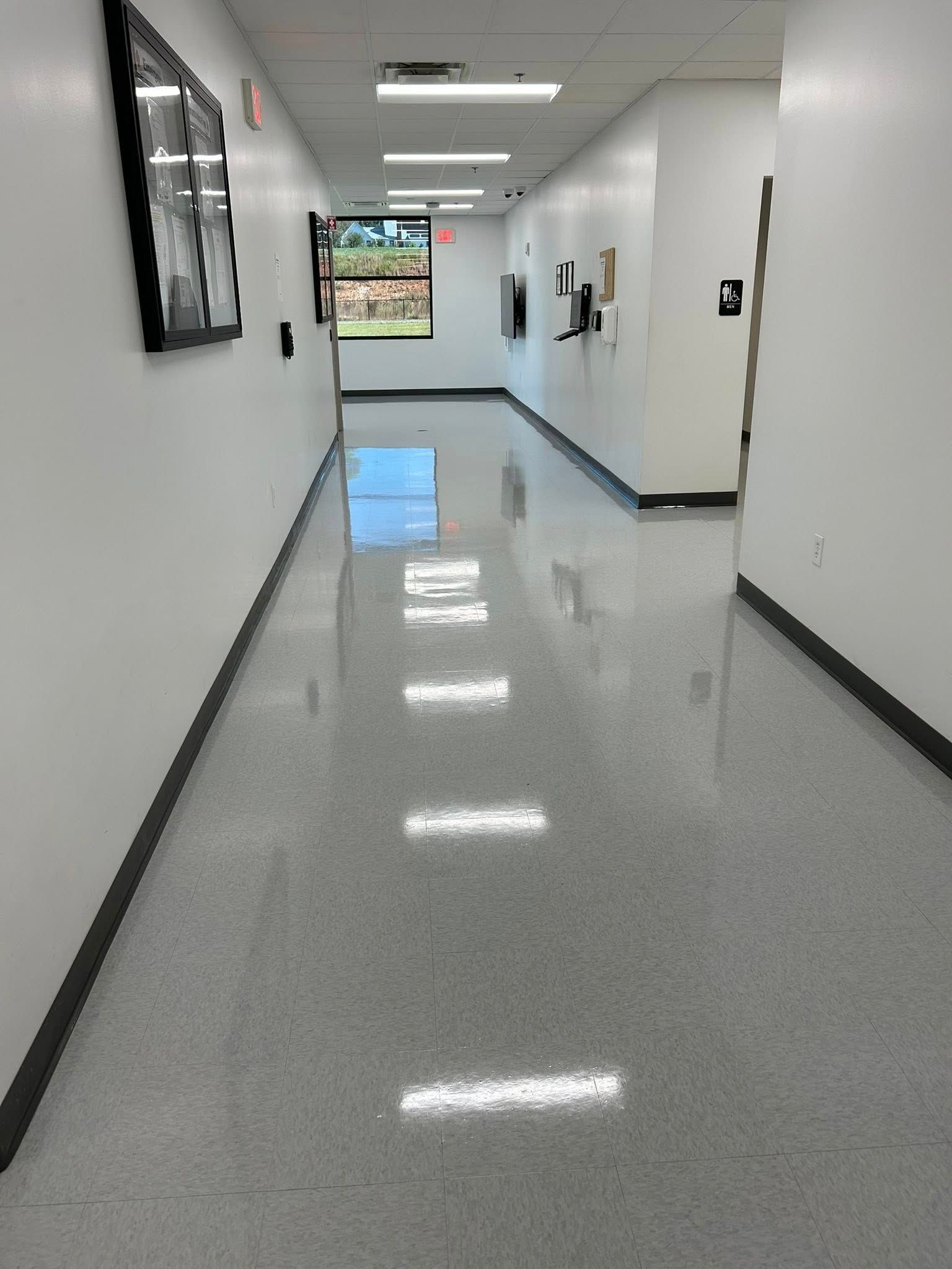Hallway with white walls, gray floor, recessed lights, and a window at the end.