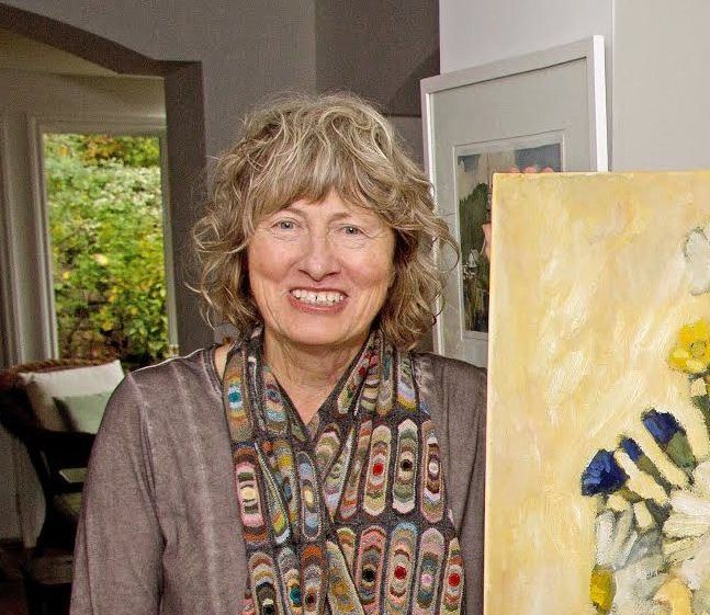 A woman is holding a painting of flowers and smiling.