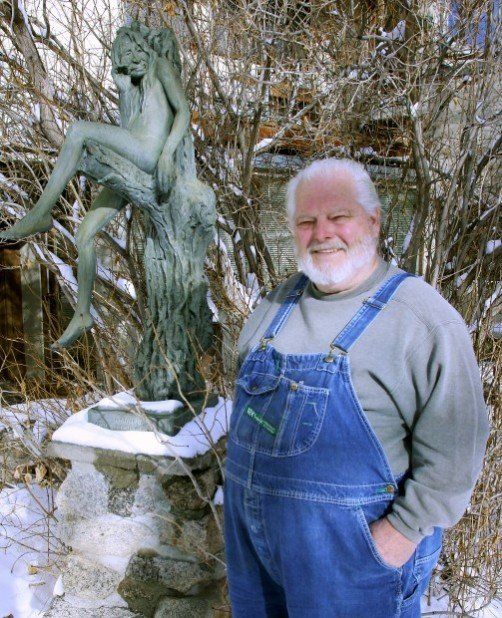 A man in overalls stands in front of a statue