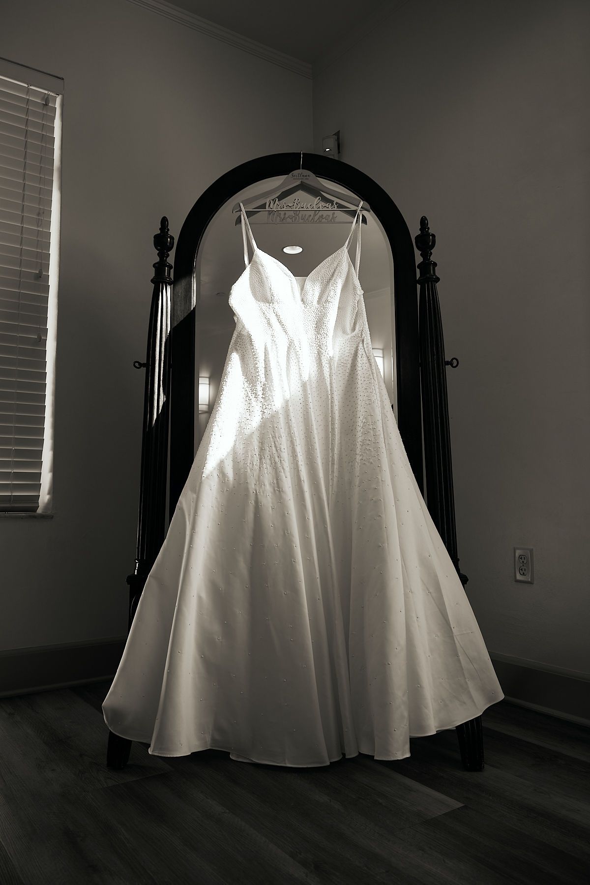 A wedding dress is hanging in front of a mirror.