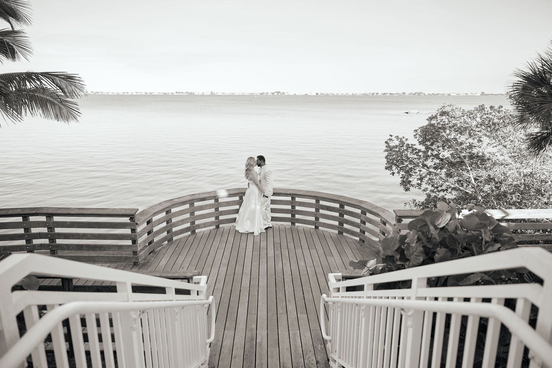 A black and white photo of a bride and groom on a pier overlooking the water.