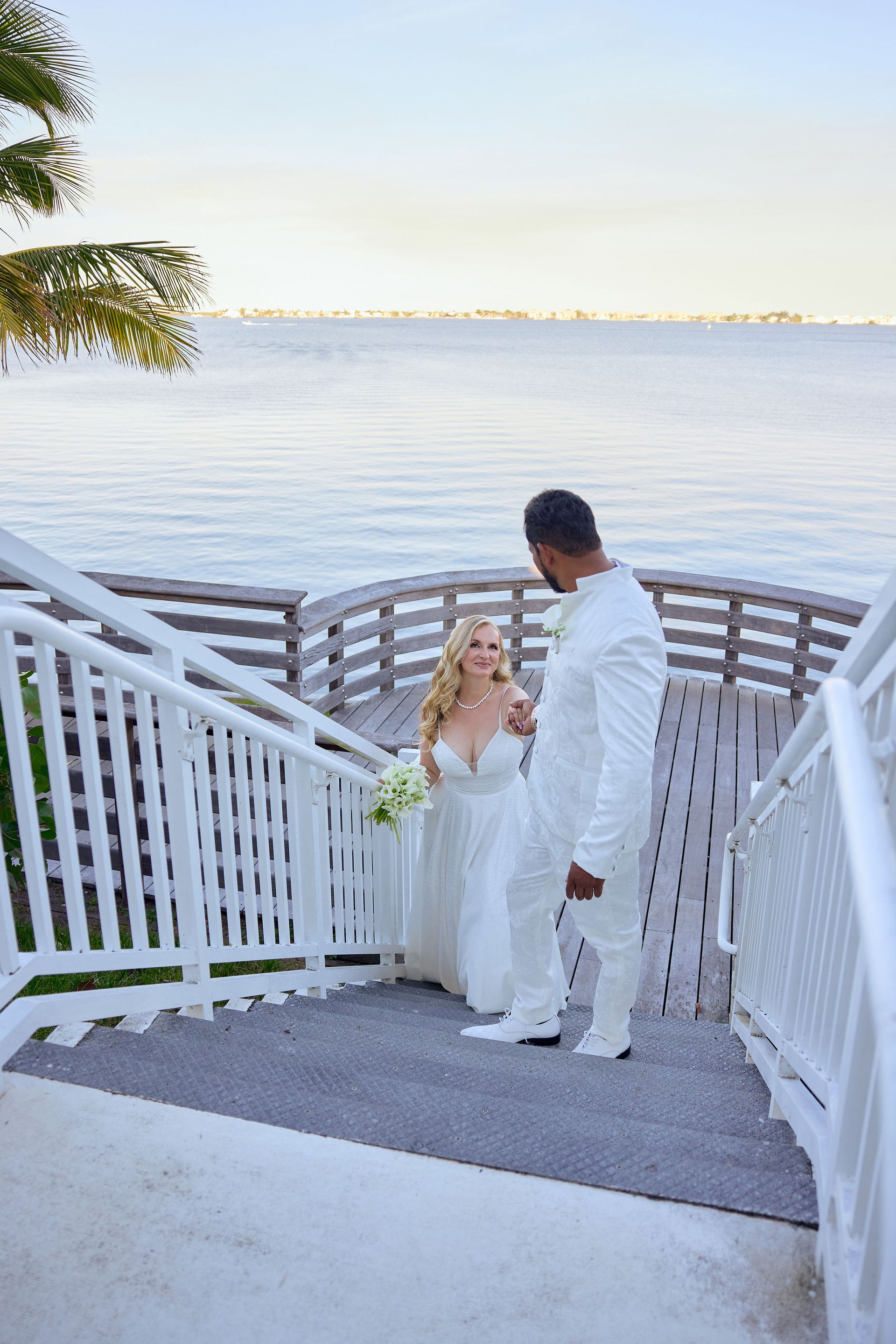 A bride and groom are walking down stairs overlooking the ocean.