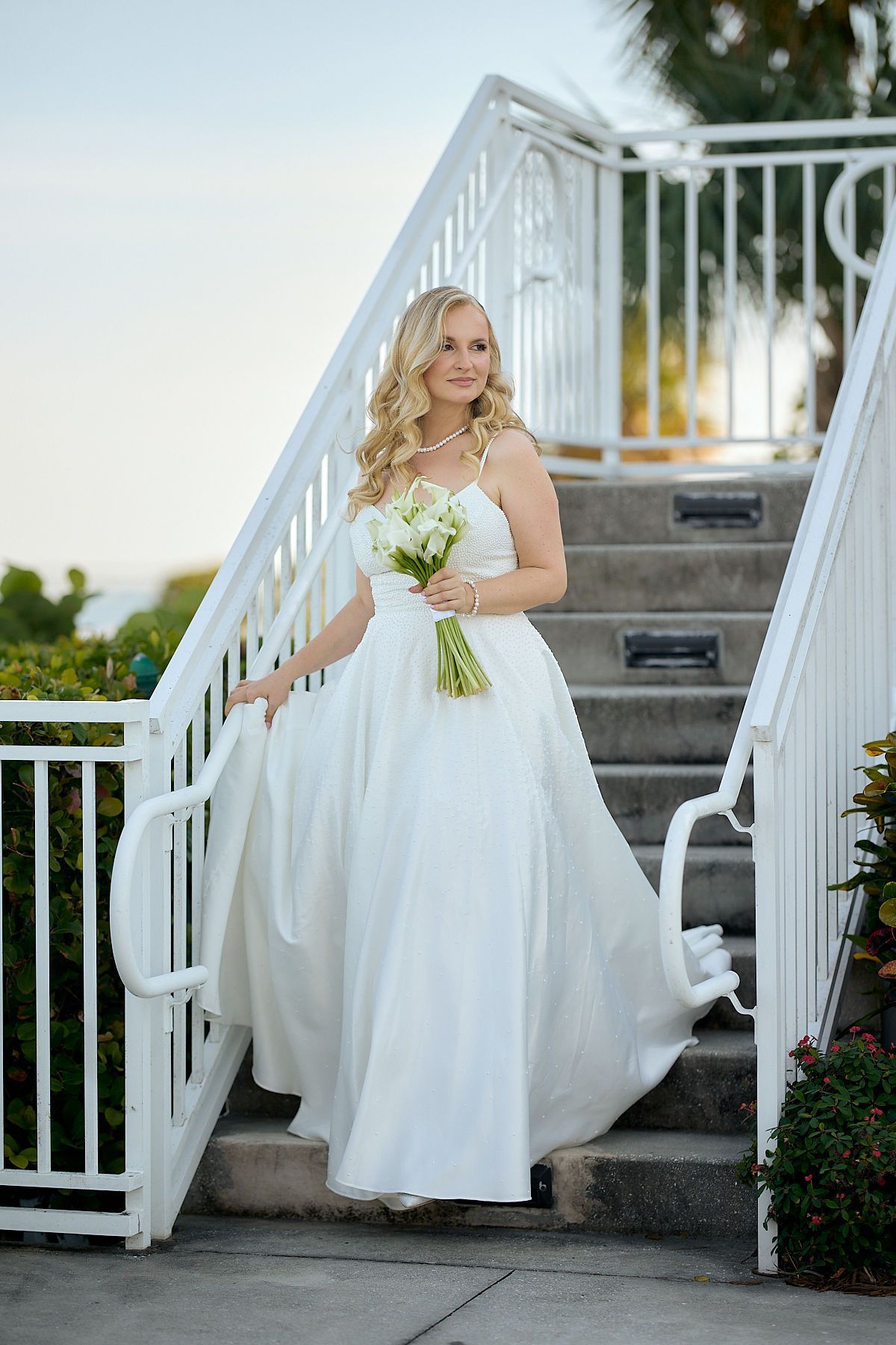 A bride in a white dress is walking down a set of stairs holding a bouquet of flowers.