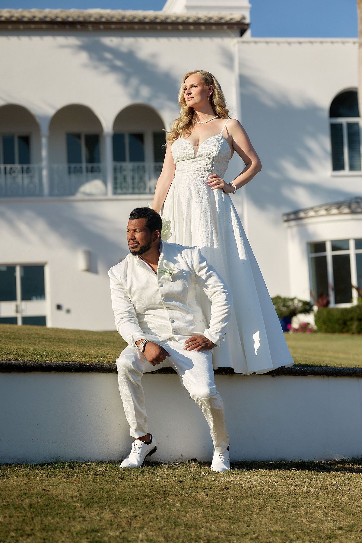 A bride and groom are posing for a picture in front of a white building.