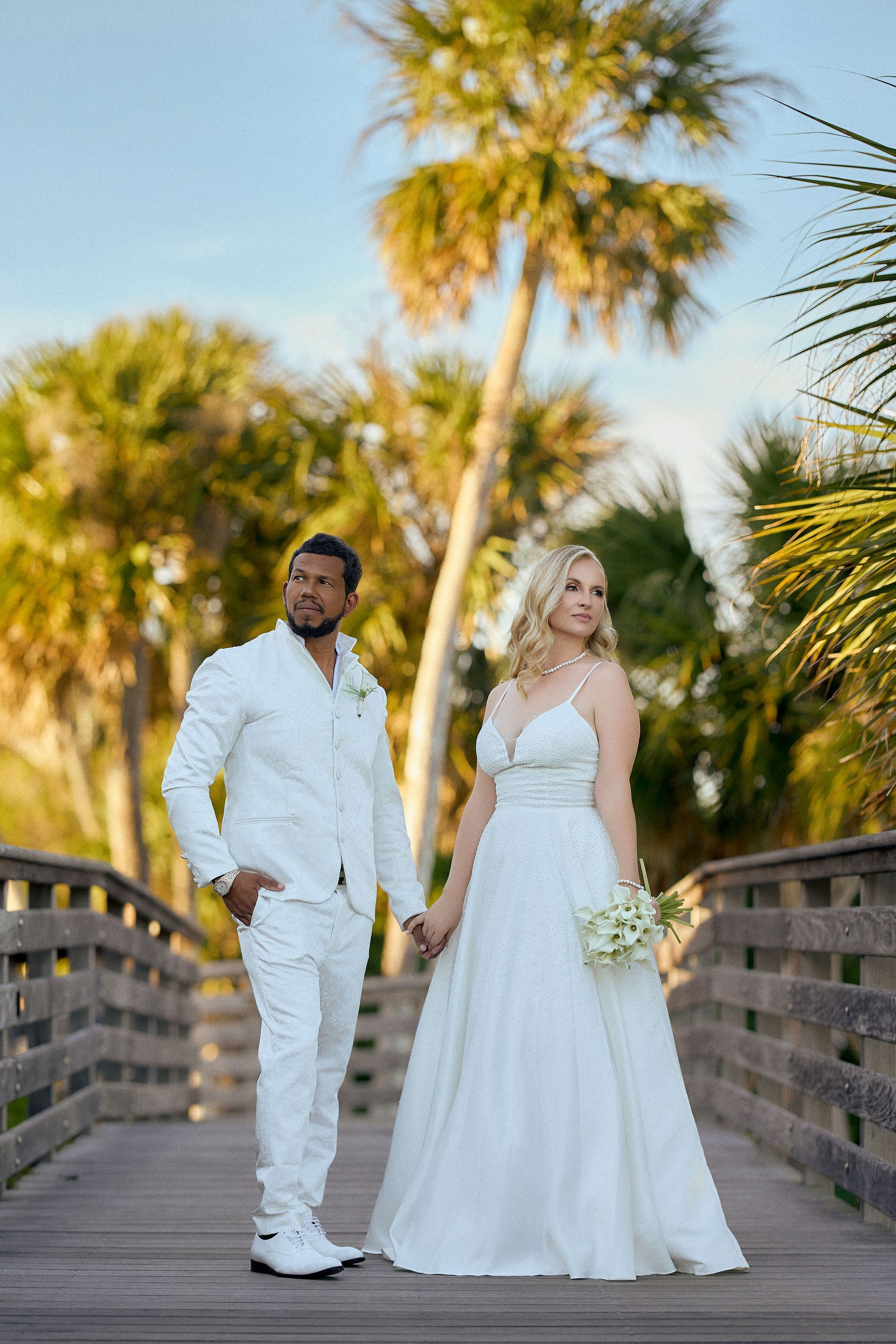 A bride and groom are standing on a wooden bridge holding hands.