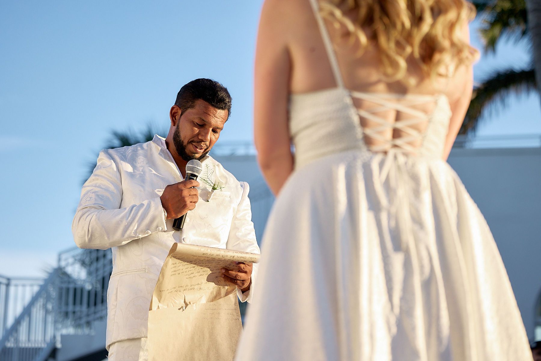 A man in a white suit is giving a speech to a bride in a white dress.