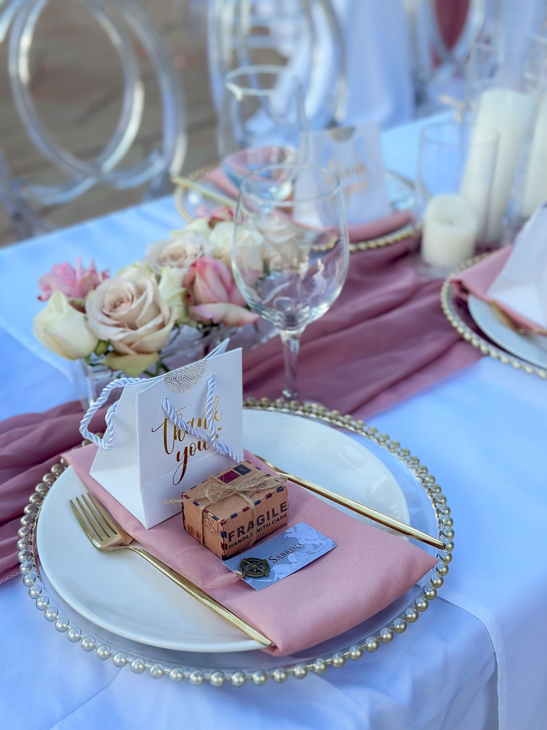 A table set for a wedding reception with plates , napkins , utensils , flowers and a thank you card.