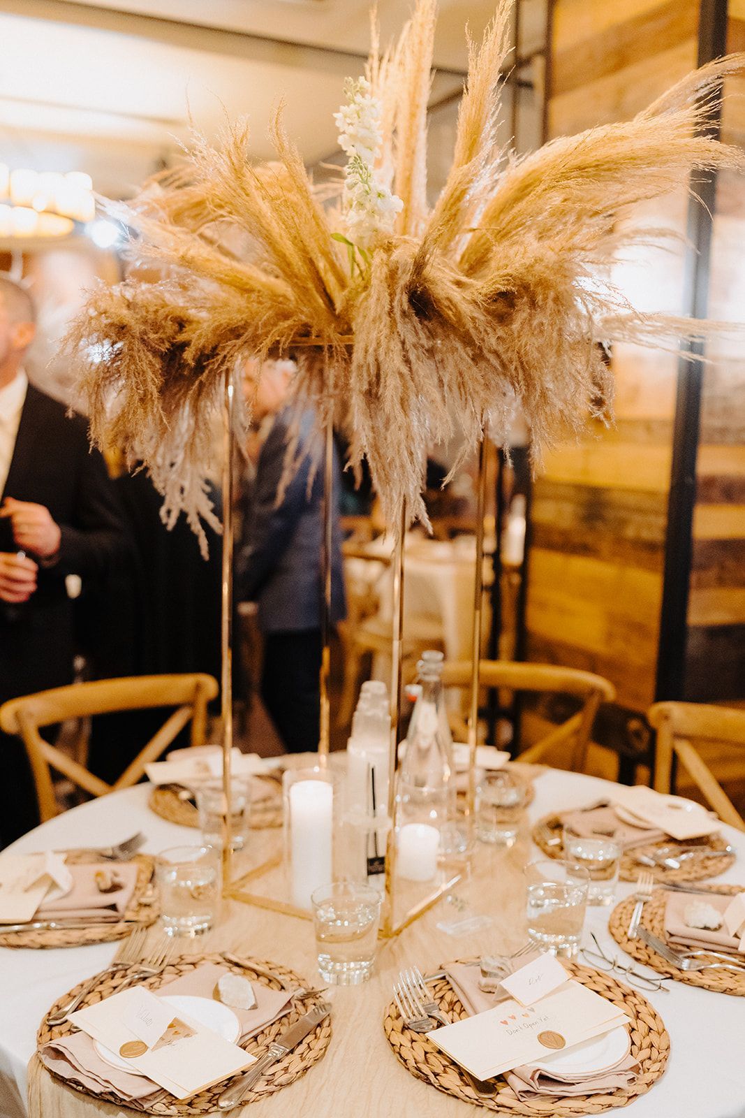 A table set for a wedding reception with a tall vase filled with dried flowers.
