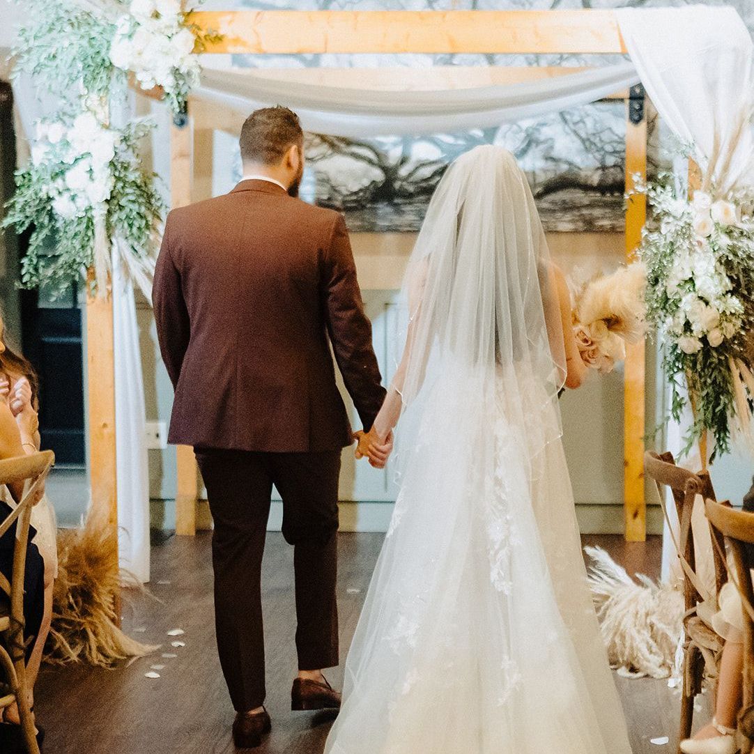 A bride and groom are walking down the aisle holding hands.