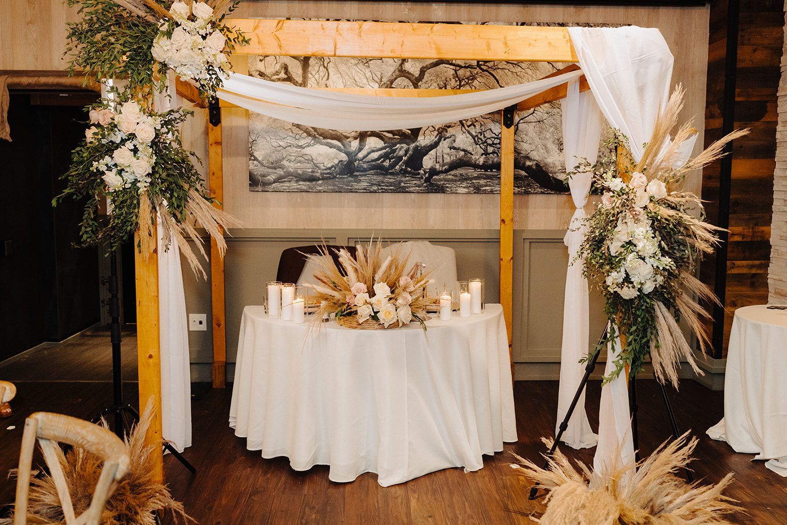 A table with a white tablecloth and candles under a wooden arch.