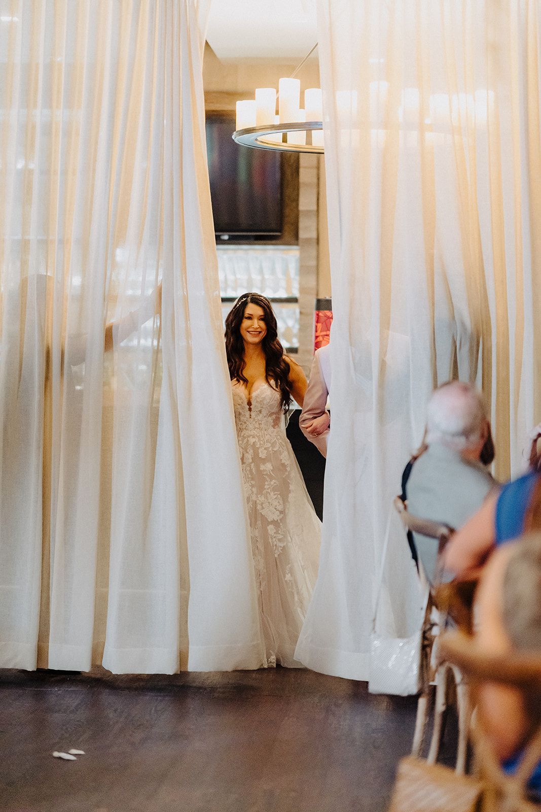 A bride in a wedding dress is standing in front of a white curtain.