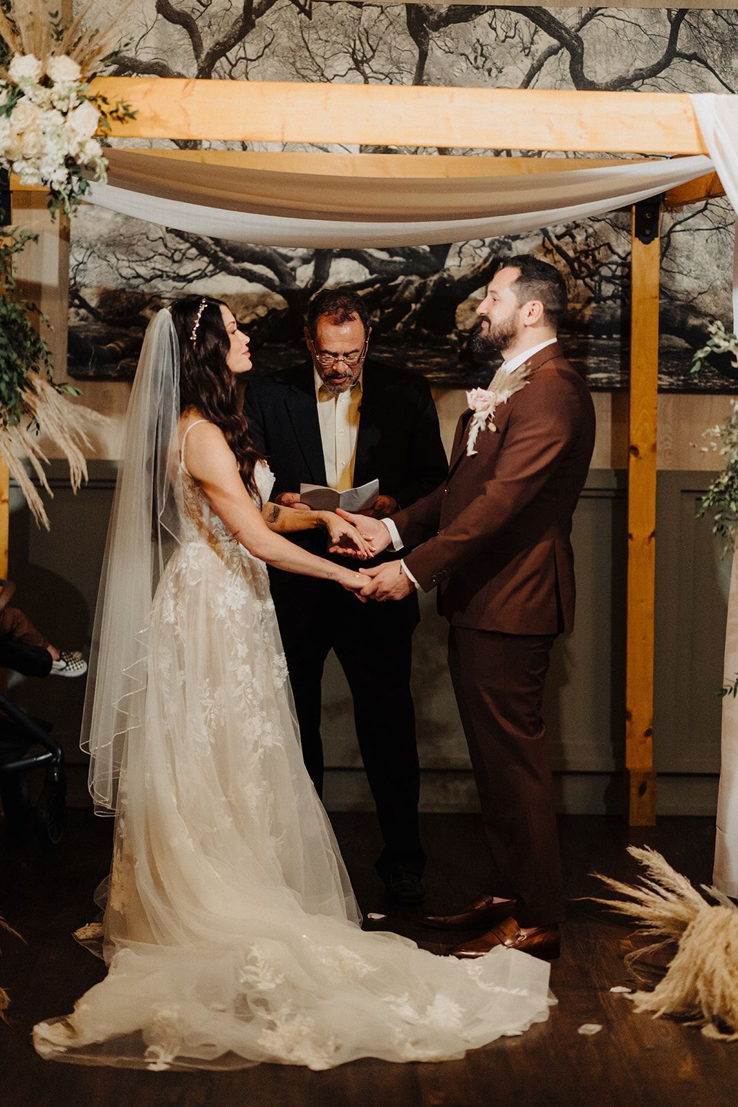 A bride and groom are holding hands during their wedding ceremony under a canopy.