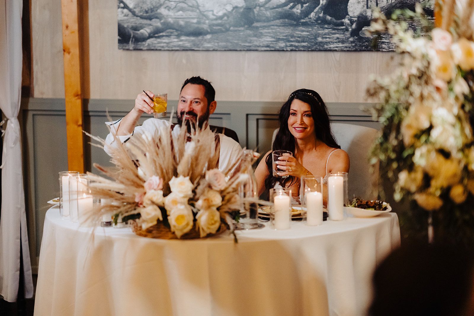 A man and a woman are sitting at a table with candles and flowers.