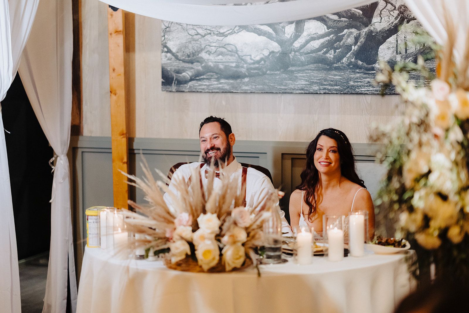 A bride and groom are sitting at a table with flowers and candles.