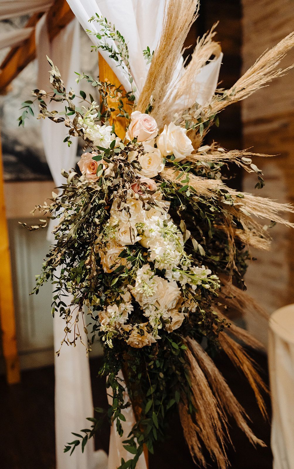 A wedding arch decorated with flowers and pampas grass.