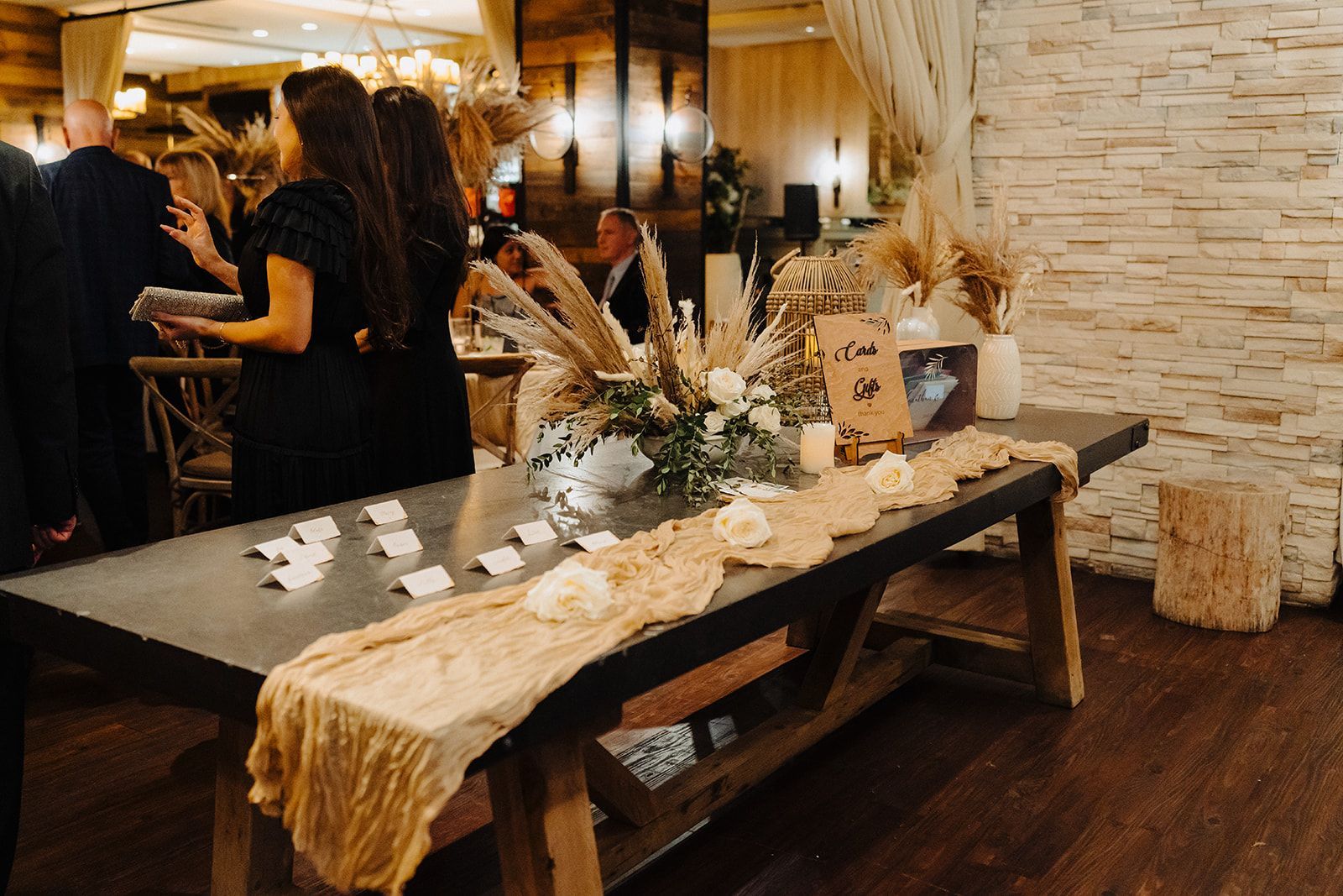 A table with flowers and candles on it in a room with people standing around it.