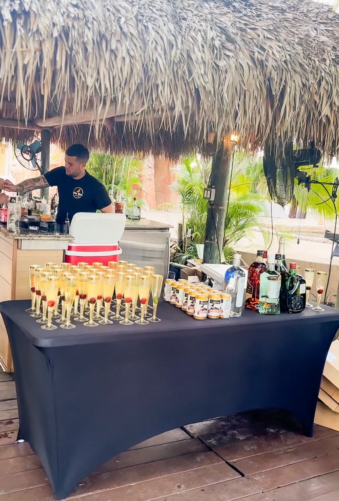 A man is preparing drinks at a bar with a thatched roof.