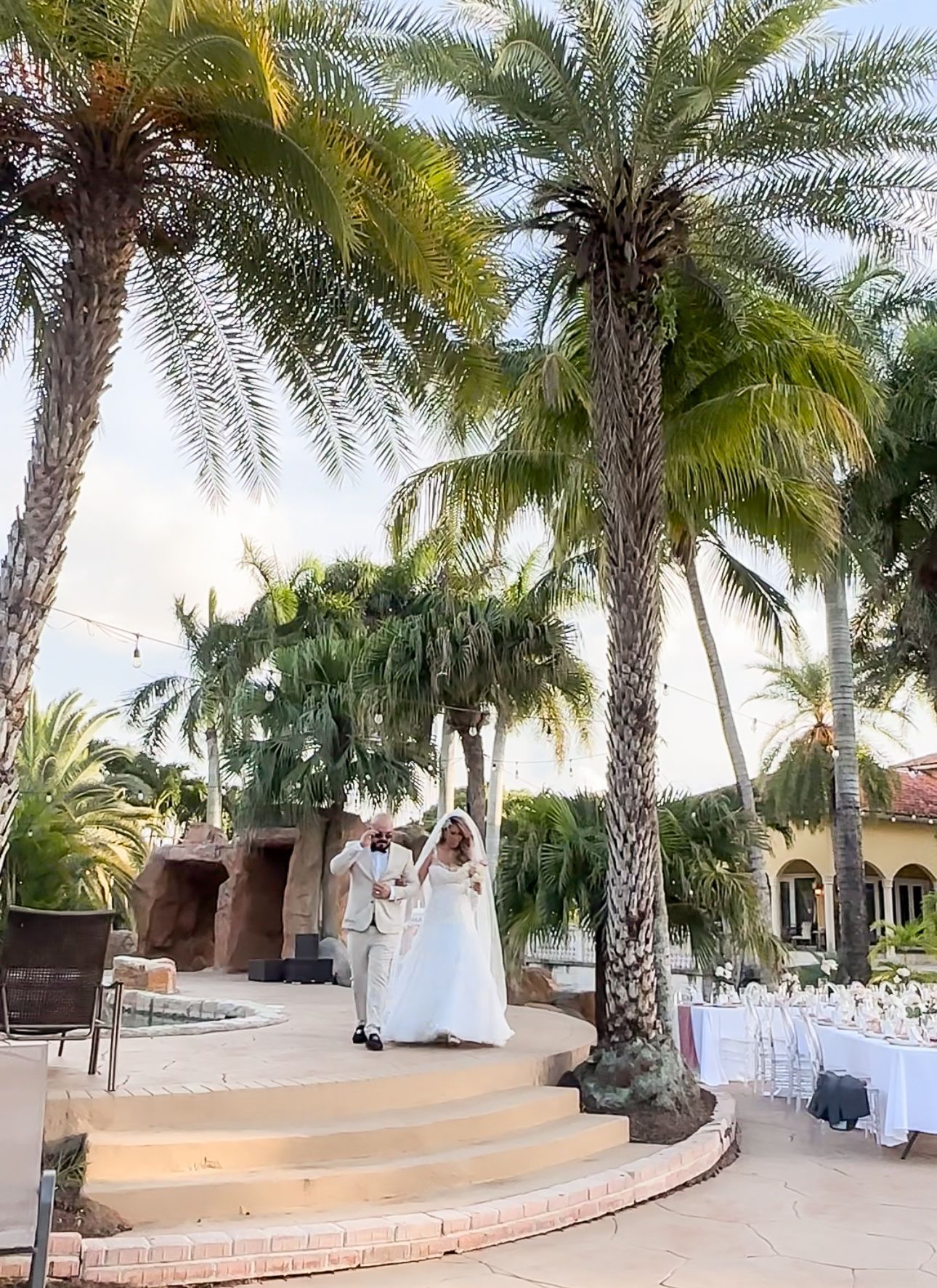 A bride and groom are walking down the aisle in front of palm trees.