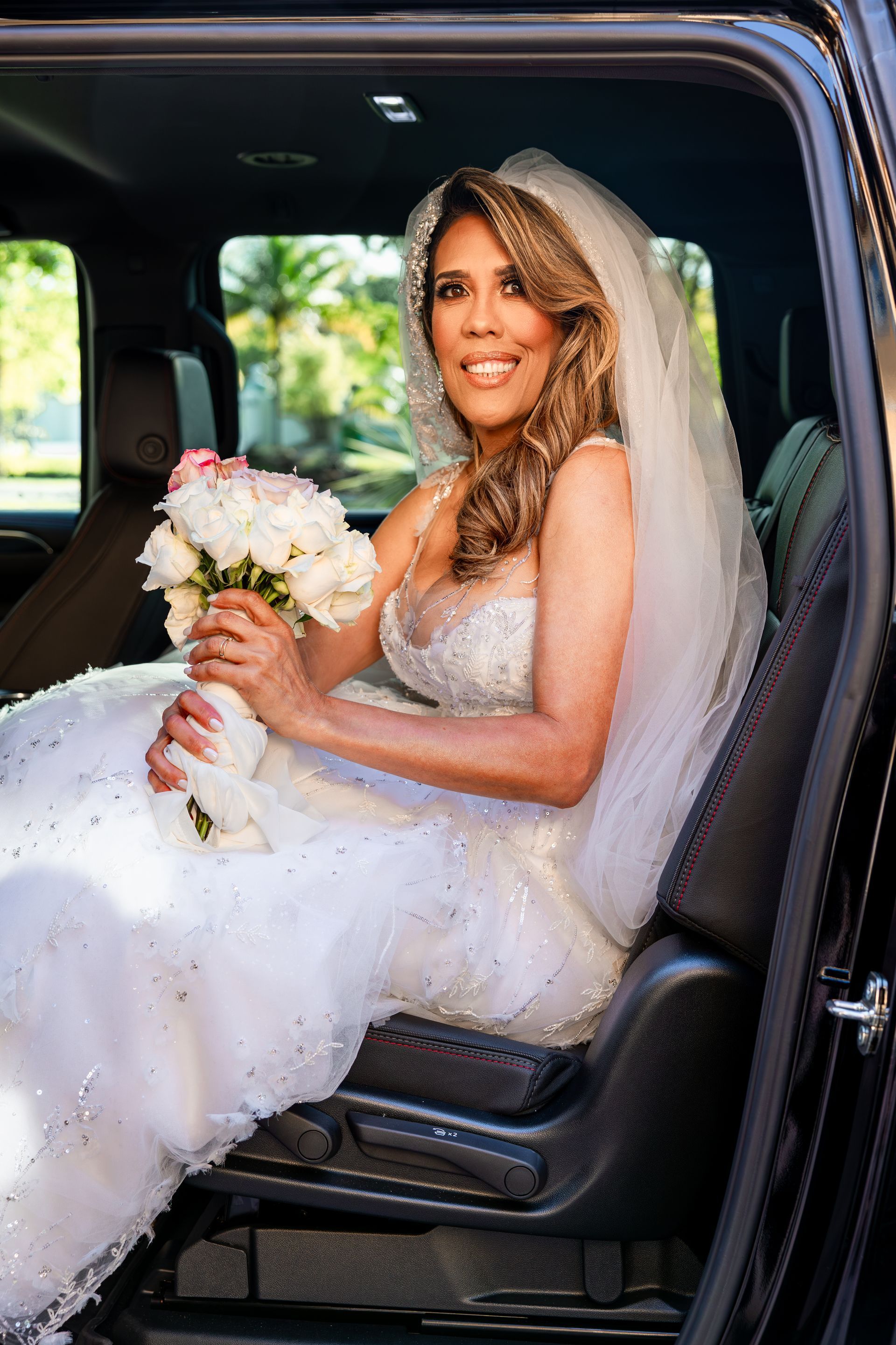 A bride is sitting in the back seat of a car holding a bouquet of flowers.