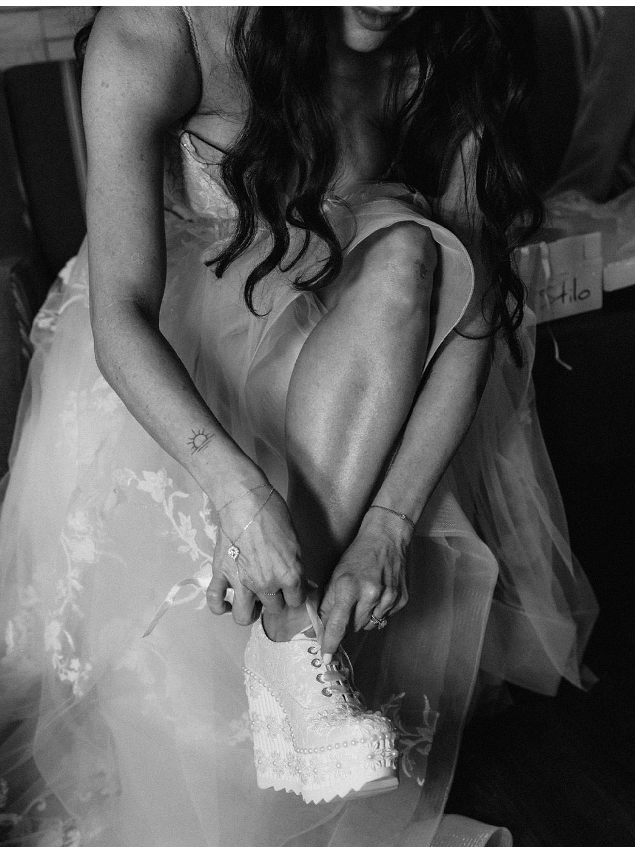 A woman in a wedding dress is tying her shoes in a black and white photo.