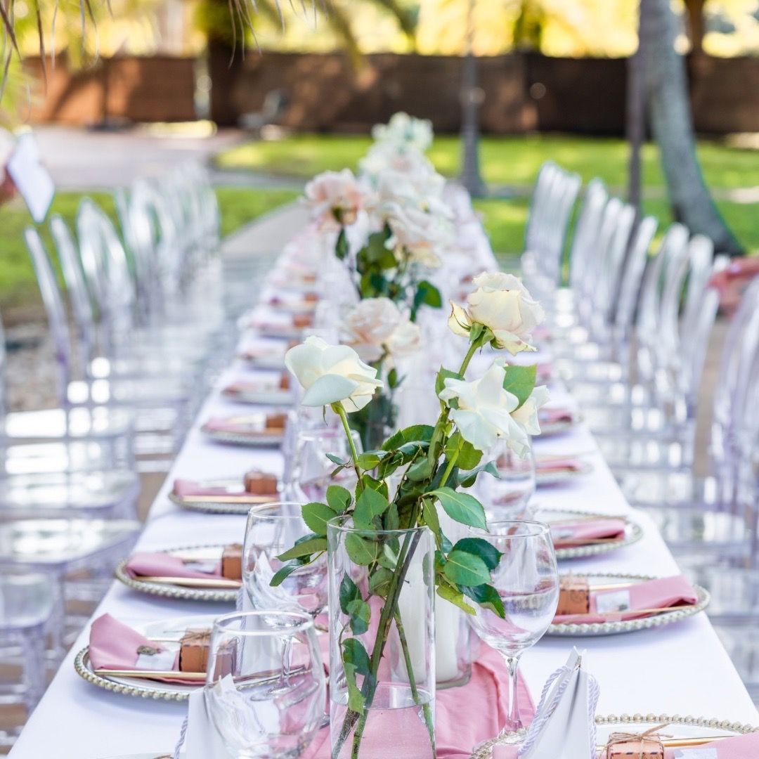 A long table with plates , glasses , napkins and flowers on it.