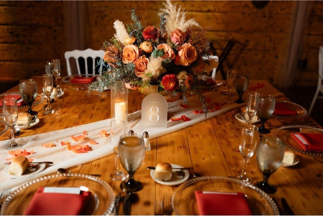 A wooden table with plates , glasses , and a vase of flowers on it.