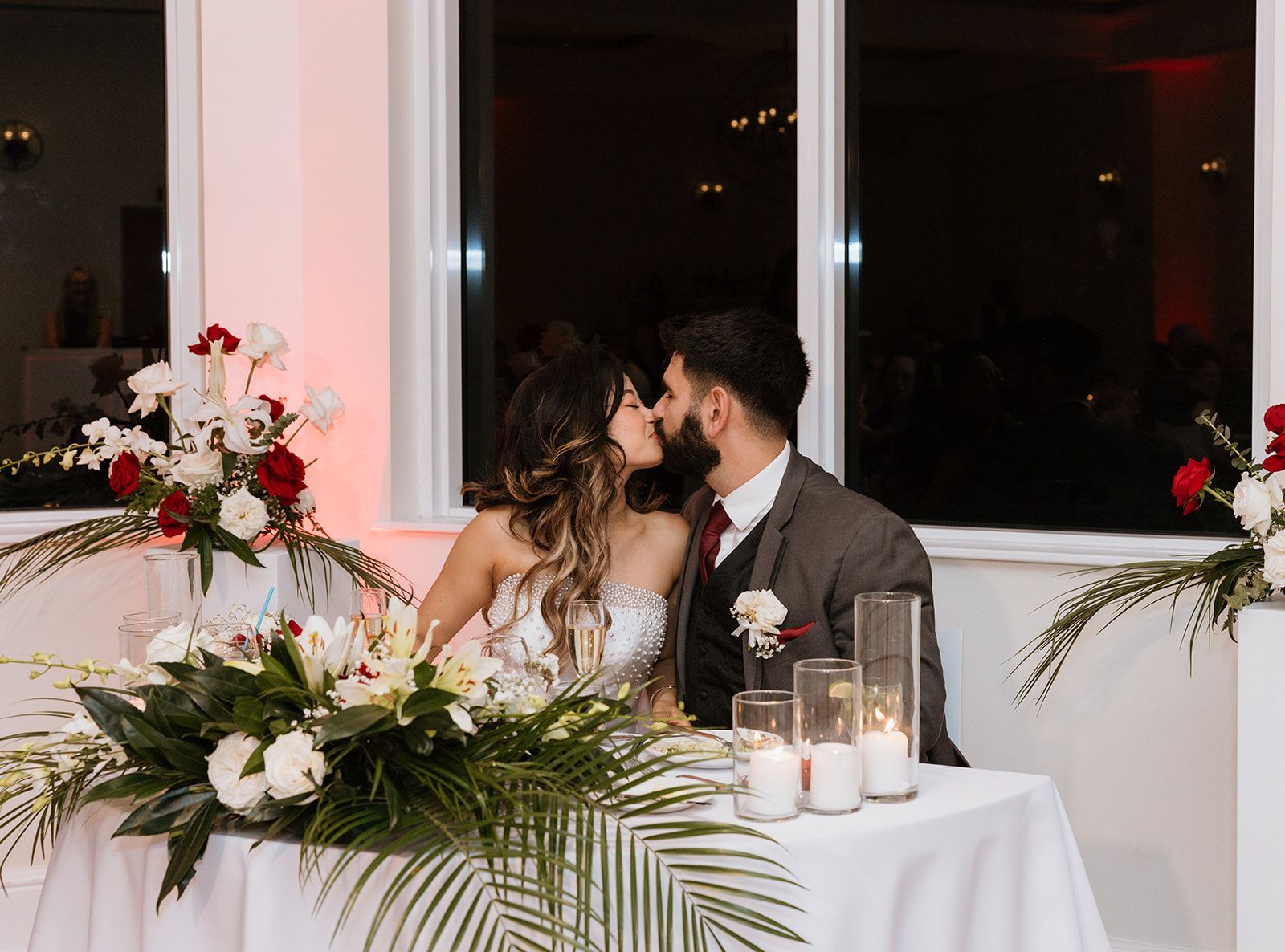 The bride and groom are kissing at the head table at their wedding reception.