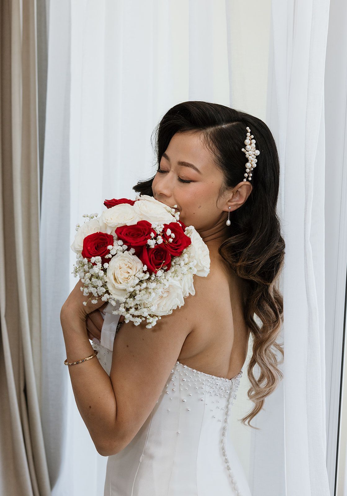 A bride in a wedding dress is holding a bouquet of red and white flowers.