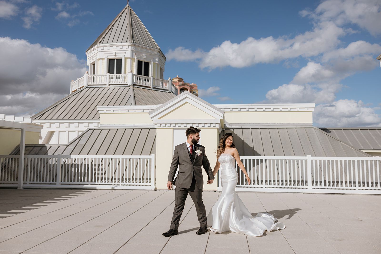 A bride and groom are walking on the roof of a building holding hands.