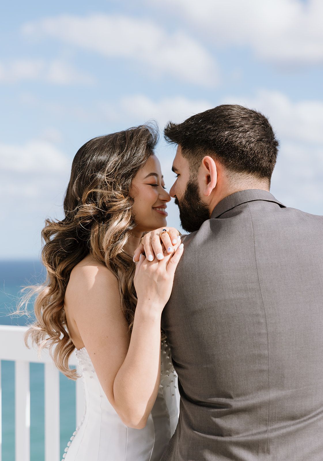 A bride and groom are kissing on a balcony overlooking the ocean.