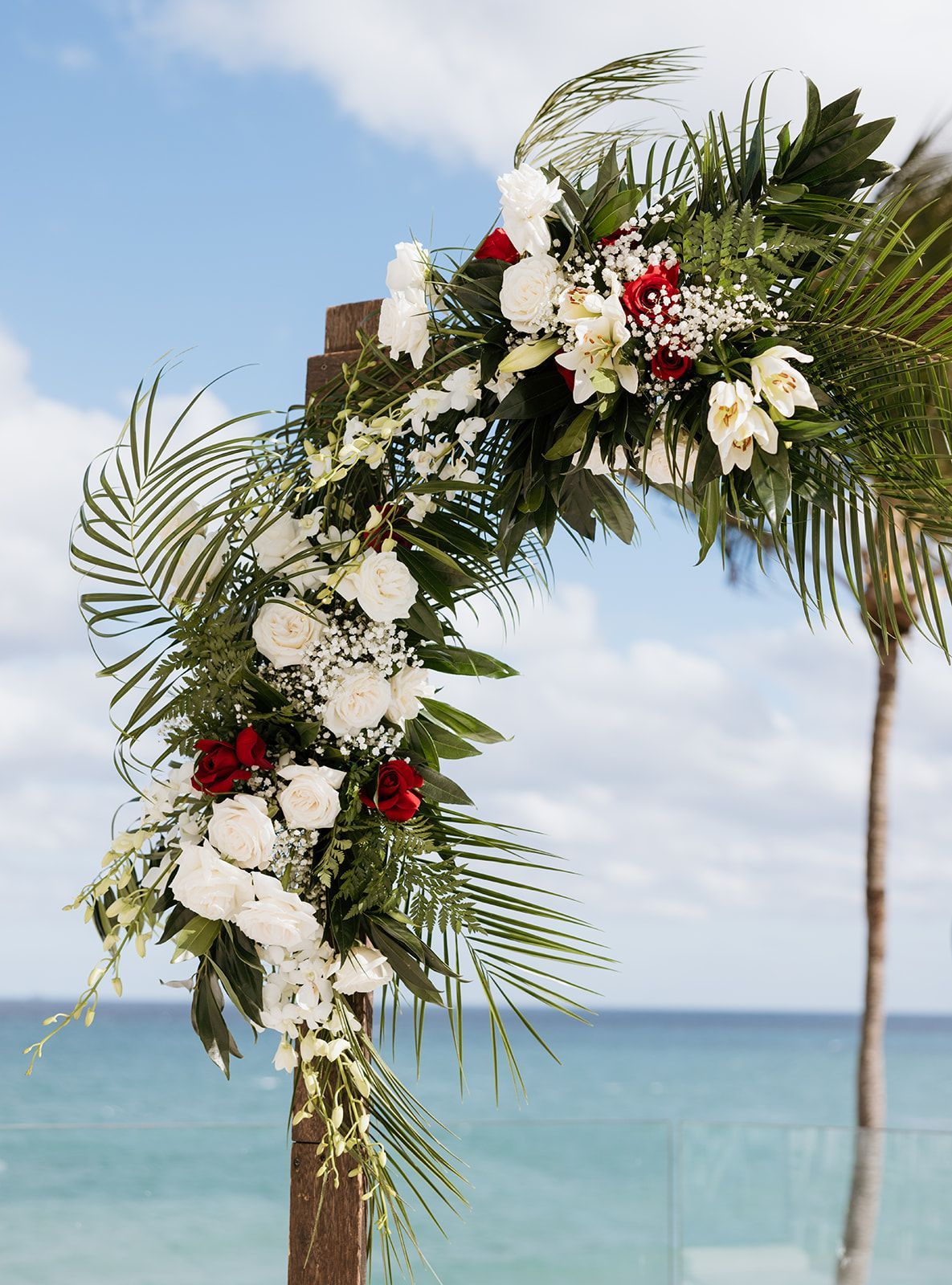 A wooden arch decorated with red and white flowers and palm leaves.