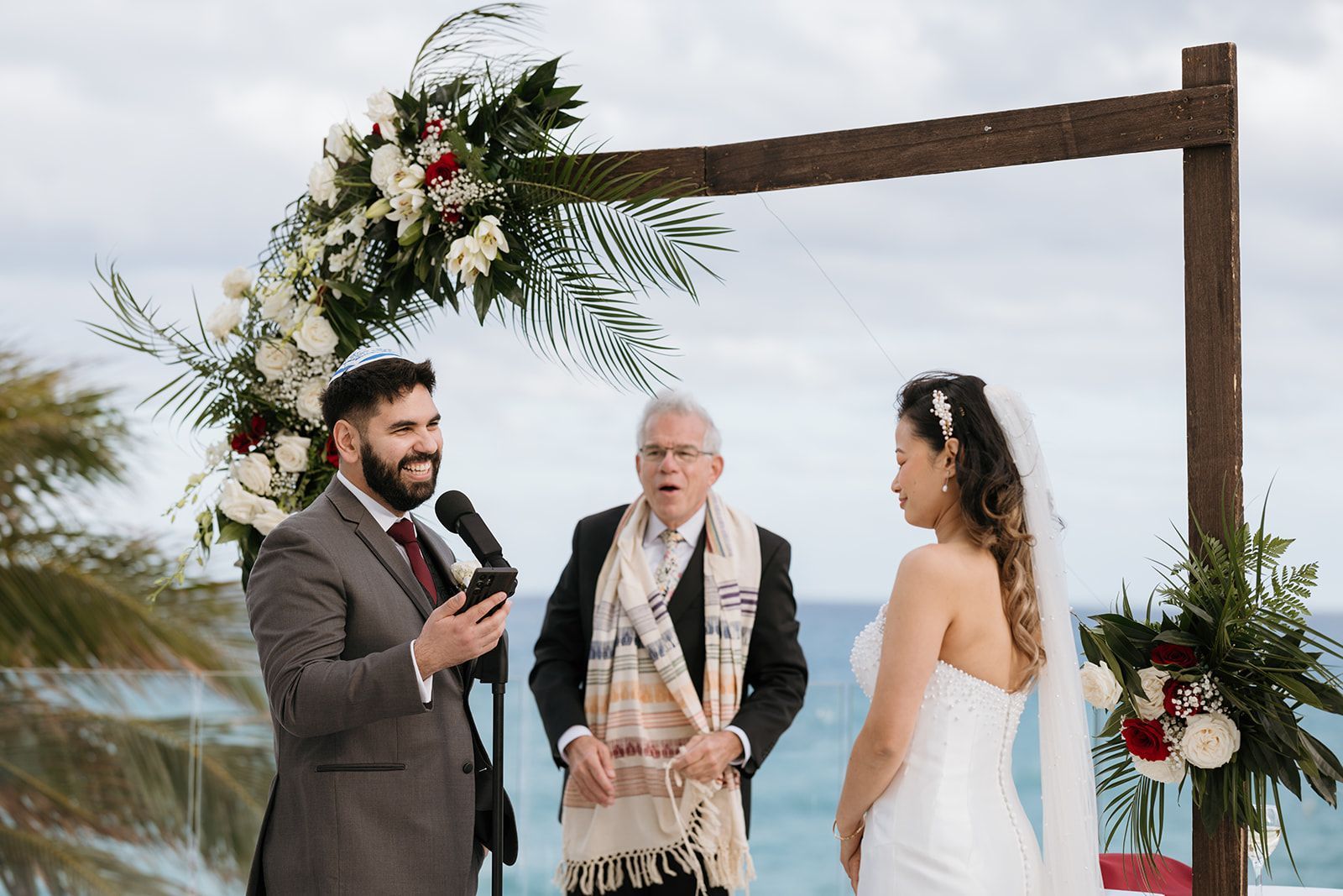 A bride and groom are standing under a wooden arch during their wedding ceremony.