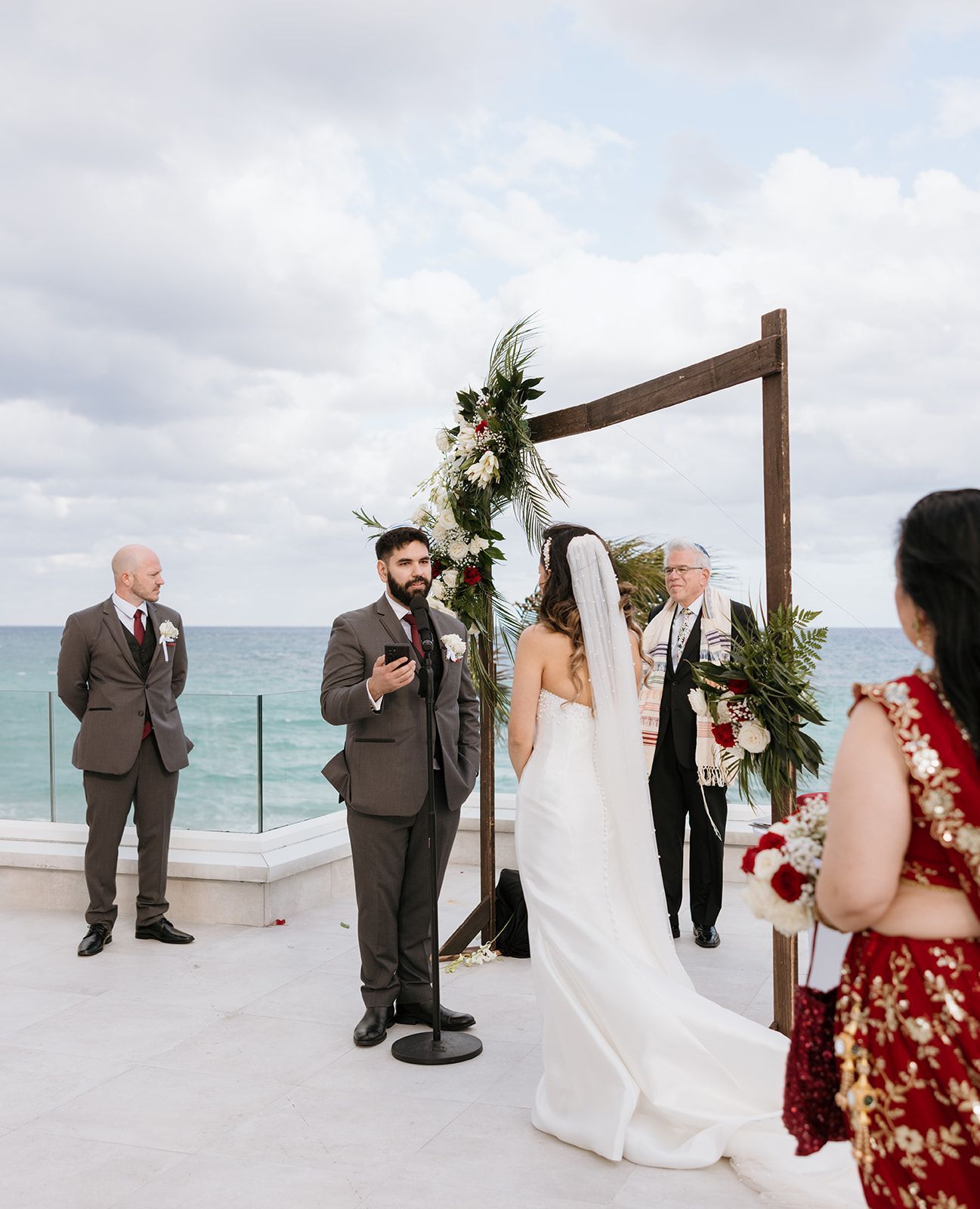 A bride and groom are standing under a wooden arch at their wedding ceremony.