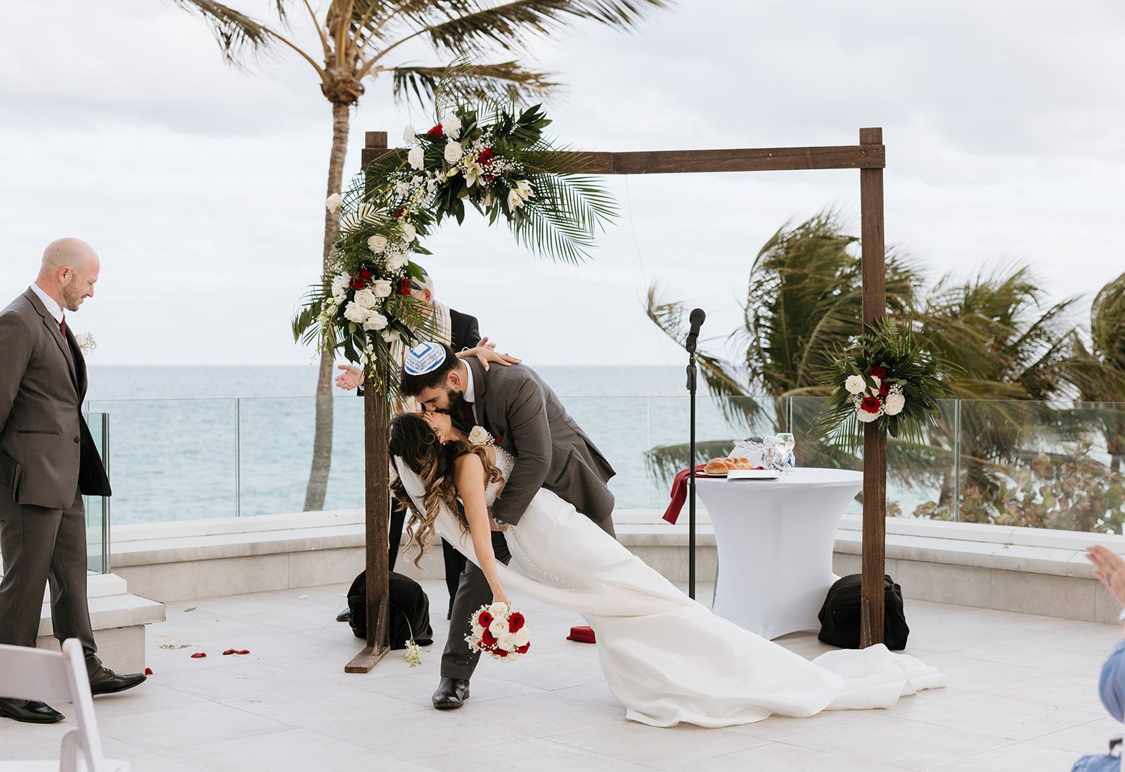 A bride and groom are kissing under a wooden arch at their wedding ceremony.