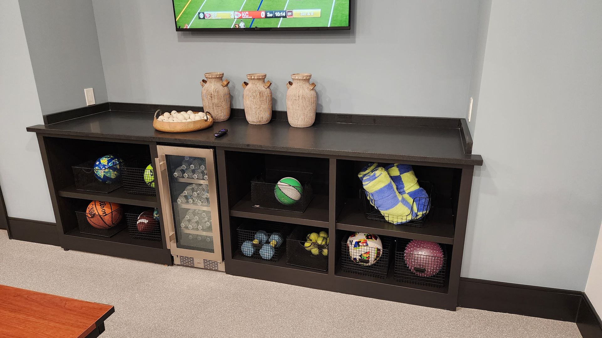 A bunch of soccer balls are sitting on a shelf in a room.