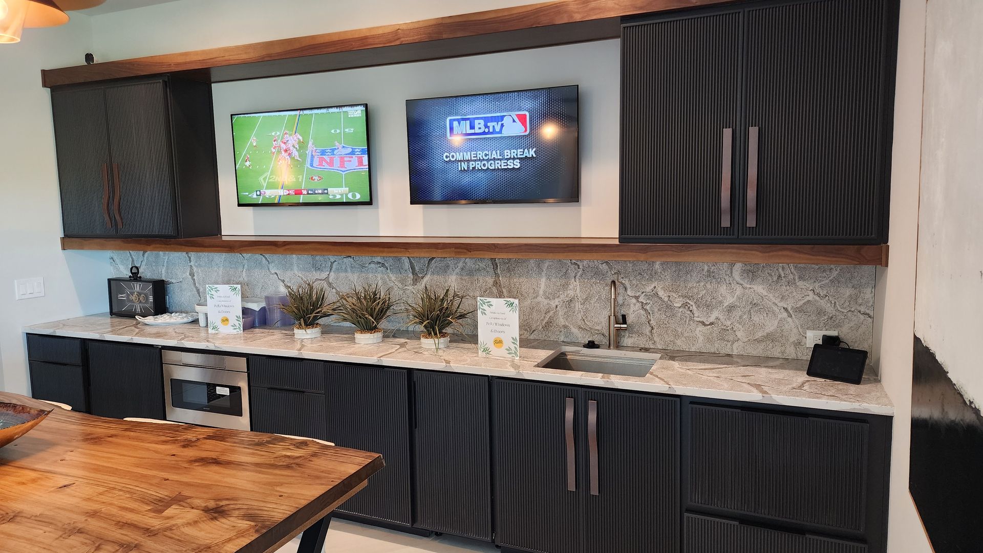 A kitchen with two flat screen tvs on the wall.