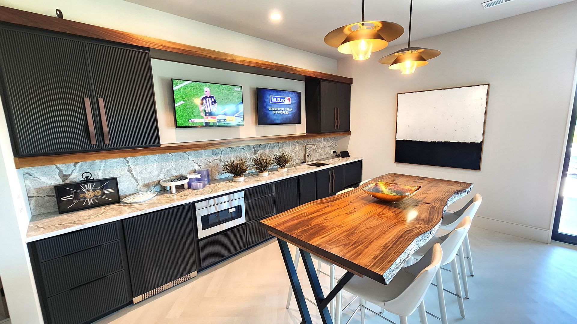A kitchen with a wooden table and chairs and two televisions on the wall.