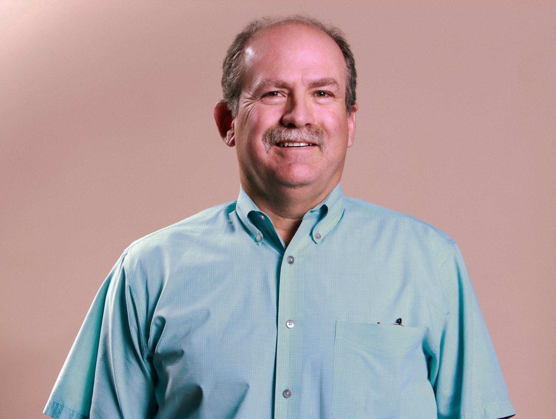 A man with a mustache is wearing a blue shirt and smiling.