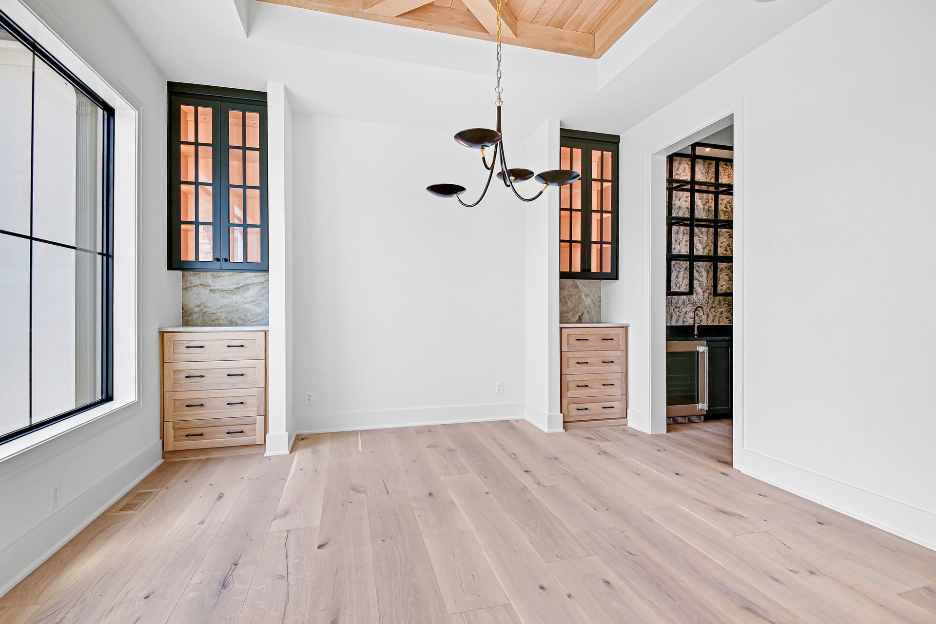 An empty room with hardwood floors and a chandelier hanging from the ceiling.