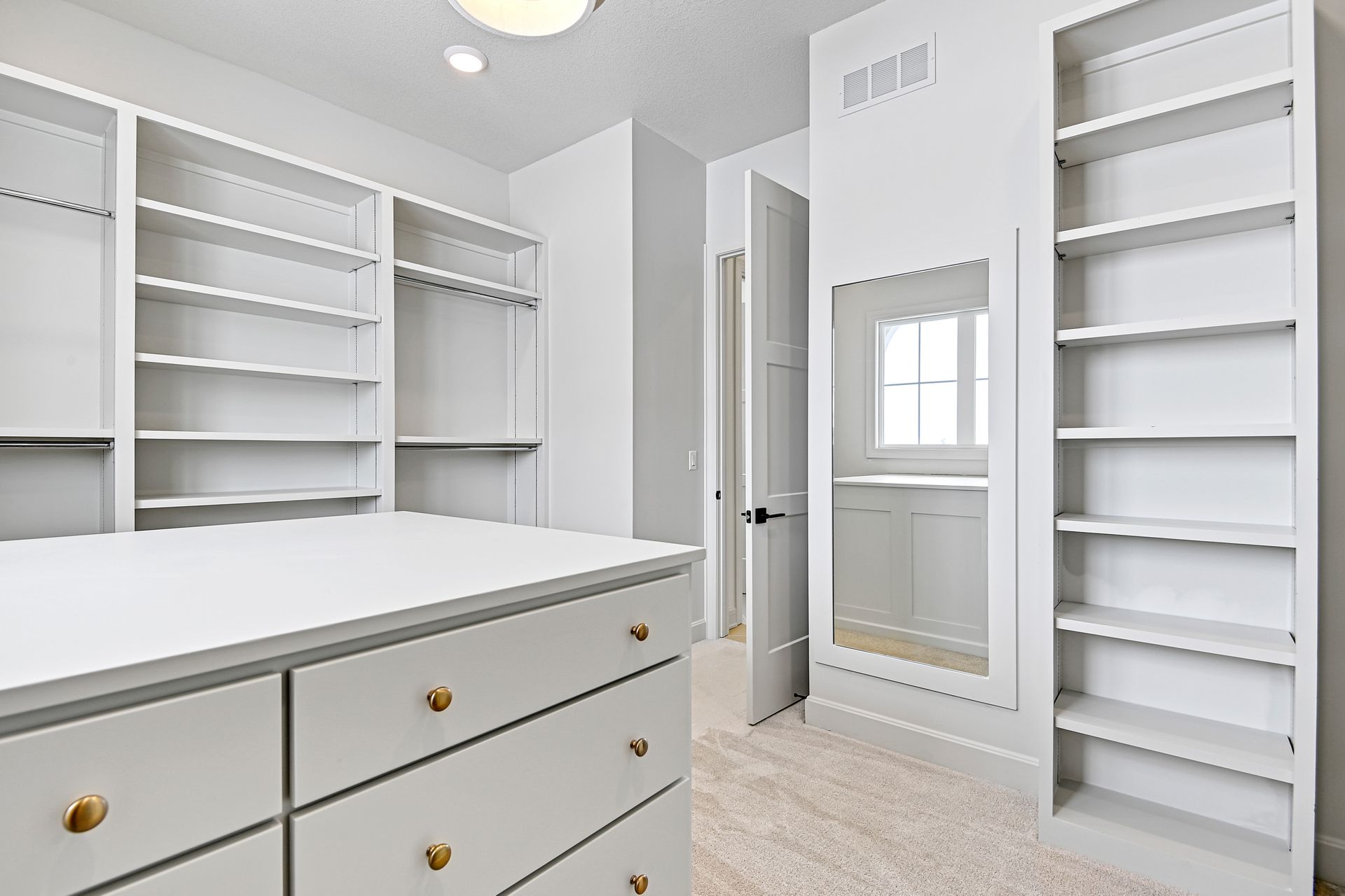 A walk in closet with lots of shelves and drawers and a mirror.