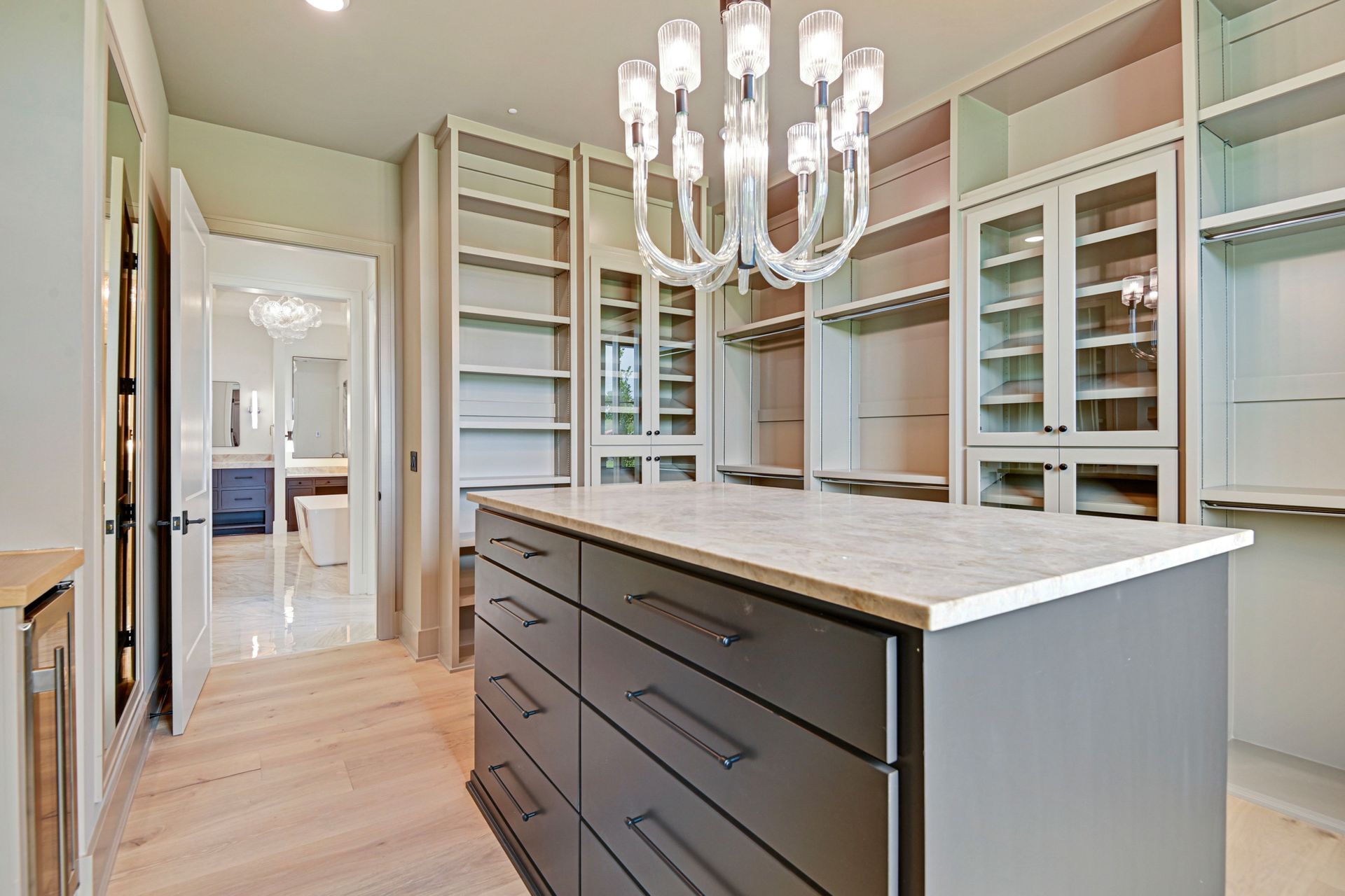 A walk in closet with a large island in the middle and a chandelier hanging from the ceiling.