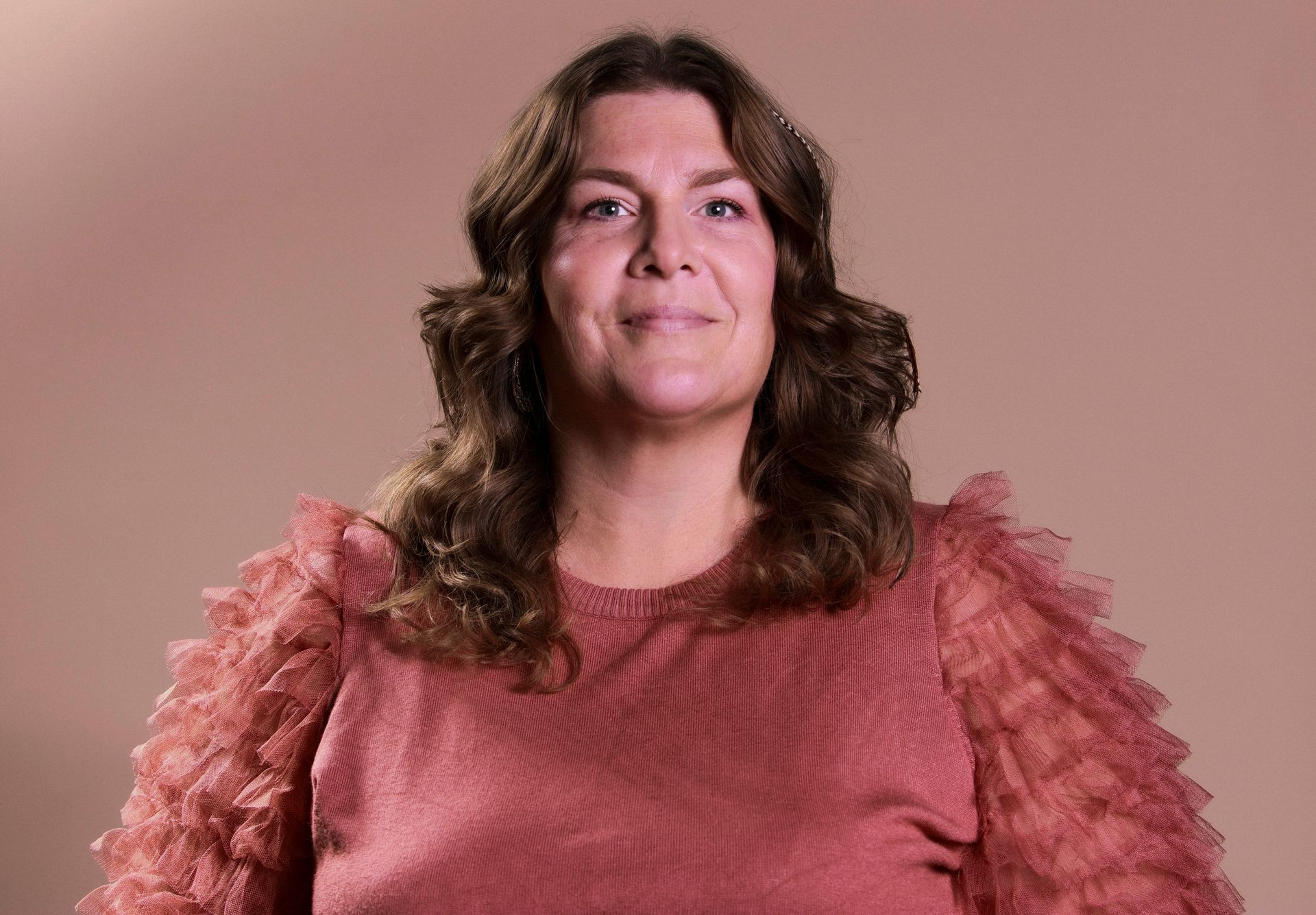 A woman in a pink sweater is smiling and looking at the camera.