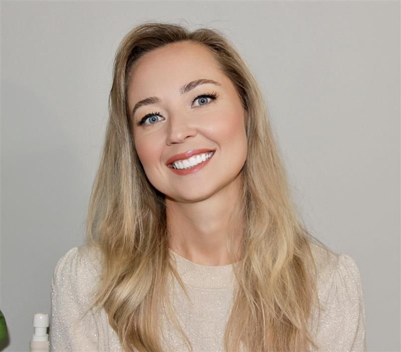 Woman with long blonde hair, smiling at camera, wearing a beige sweater.