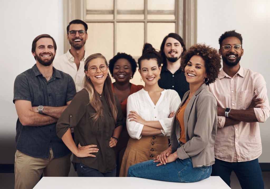 Group of smiling people posing, arms crossed, in a bright room.