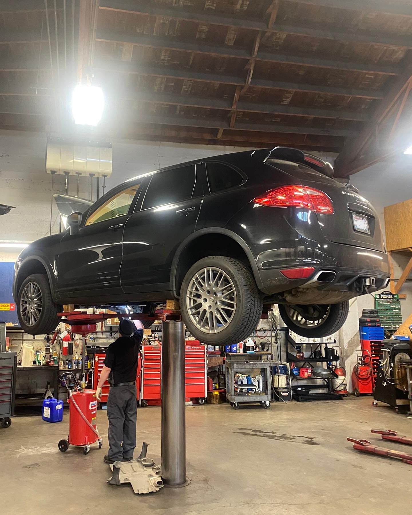 A mechanic works underneath a black SUV elevated on a lift inside a professional automotive repair shop. | West Coast Overland