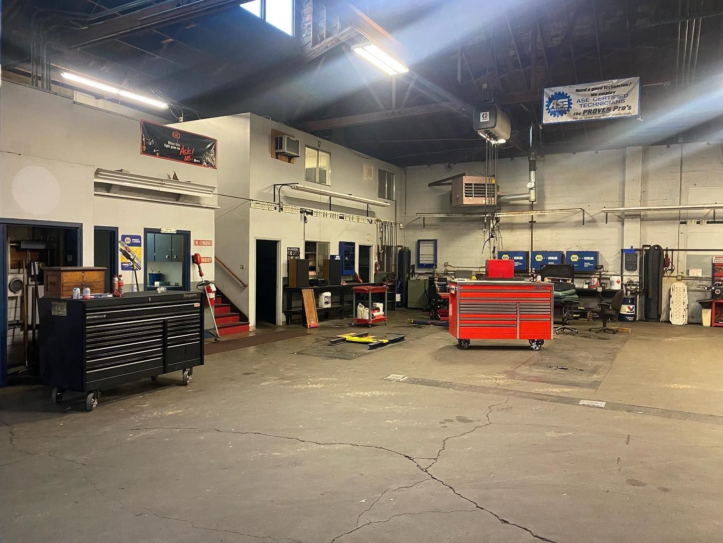 An indoor auto repair shop with concrete floors, a large black tool chest, and a red mobile tool cabinet. | West Coast Overland