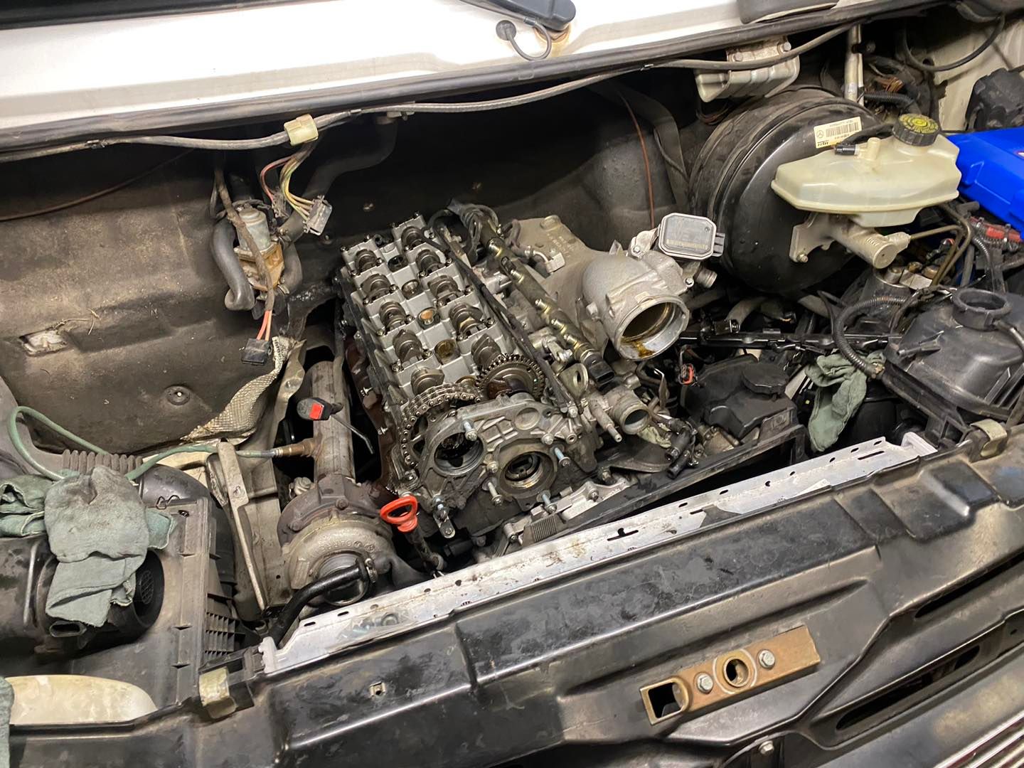 An exposed car engine with the cylinder head removed, viewed from above inside the open engine bay.