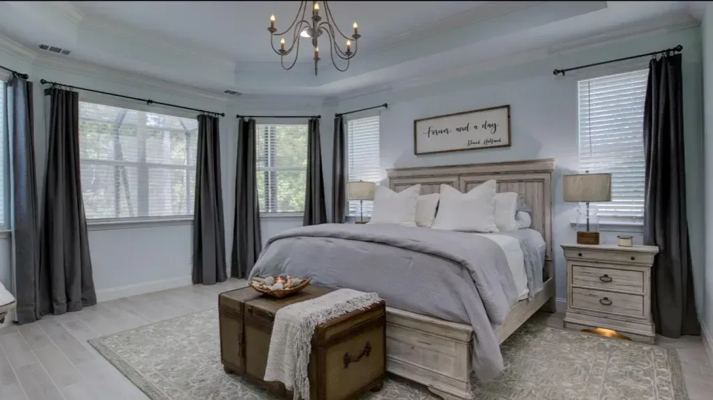 A bedroom with a large bed , nightstands , curtains and a chandelier.